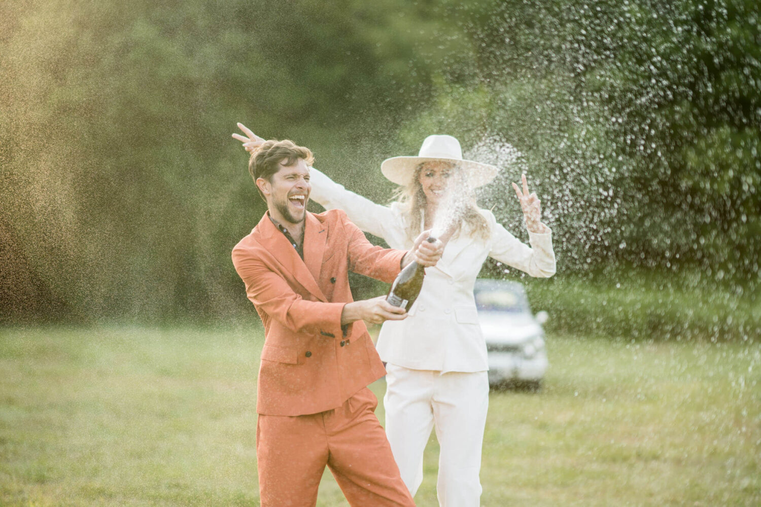 groom and bride spraying champagne in field