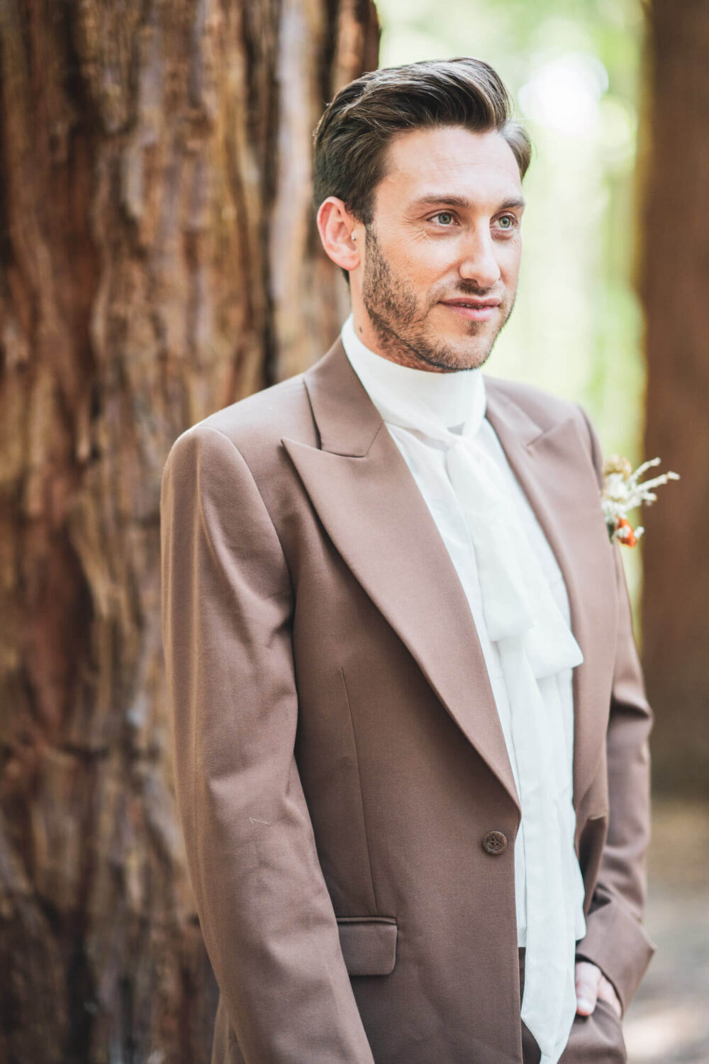 close up of groom looking left of camera with redwood tree in background
