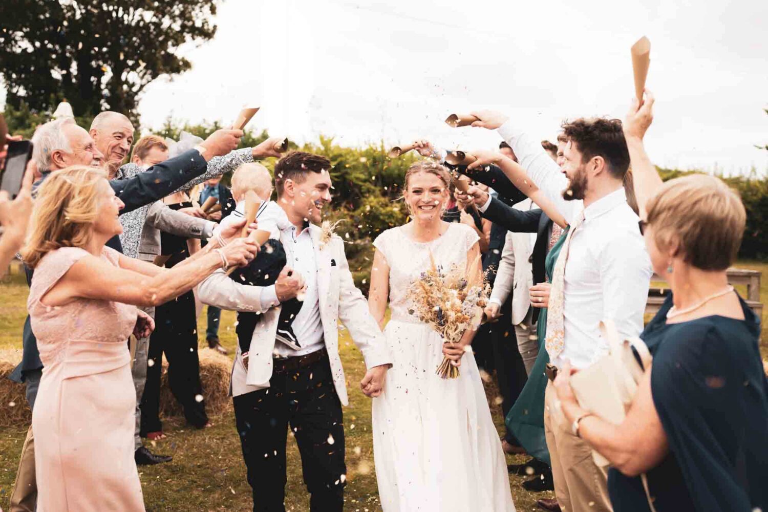 couple walking through confetti arch holding their 18 month old son