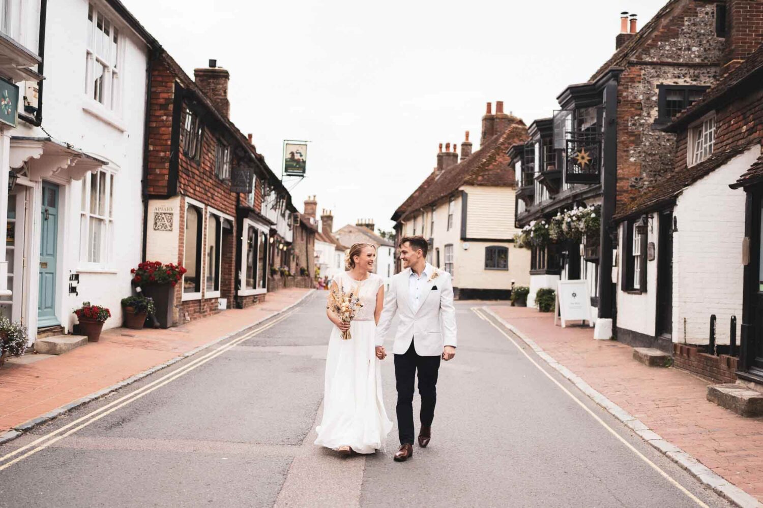 bride and groom walking hand in hand looking at each other through Alfriston high street
