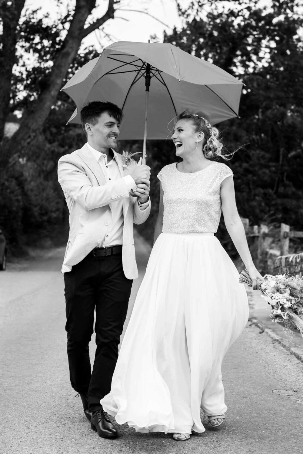 couple walking across bridge towards camera holding an umbrella