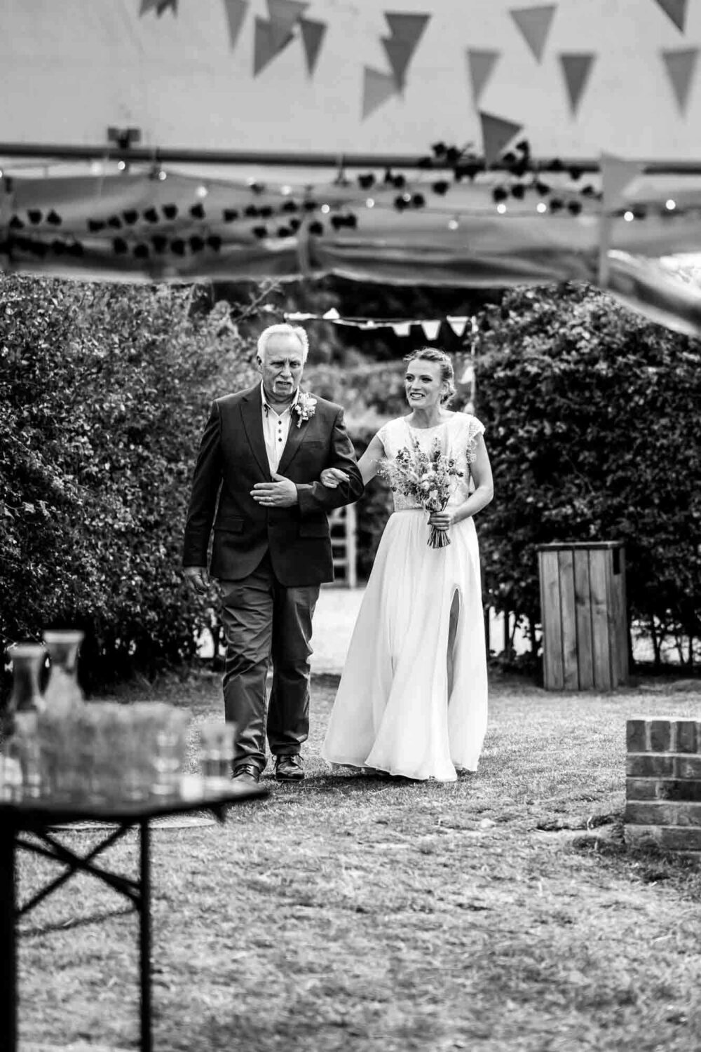 bride and father walking across grass to marquee