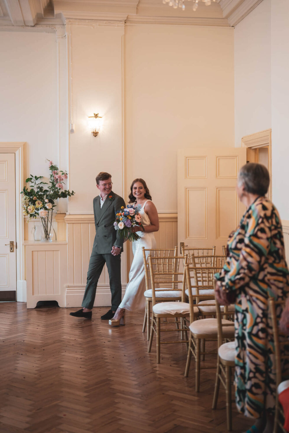 groom and bride walking into ceremony room smiling holding hands