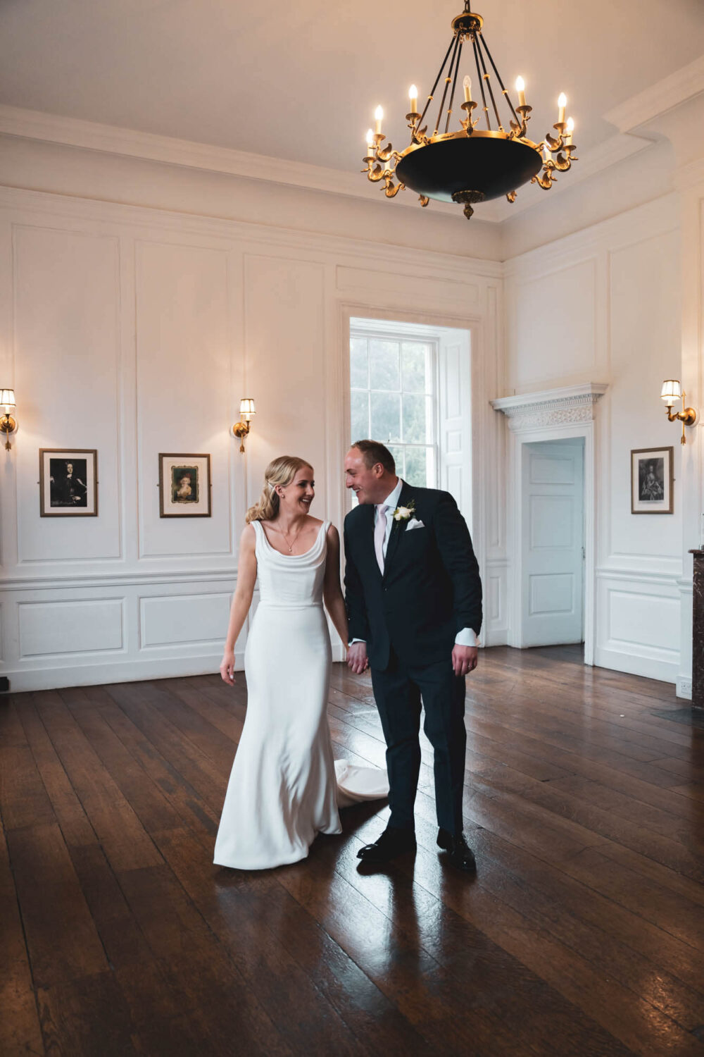 bride and groom walking through elegant Georgian room in Stanmer house looking at each other smiling