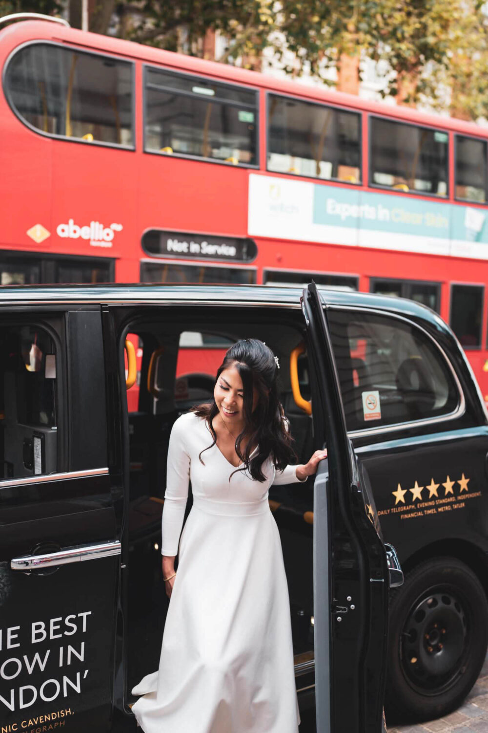bride getting out of black cab with red London bus driving passed her