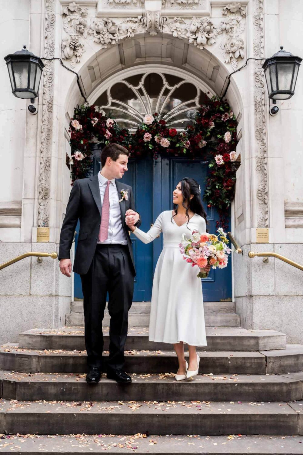 bride and groom walk down steps of Chelsea old town hall hand in hand looking at each other