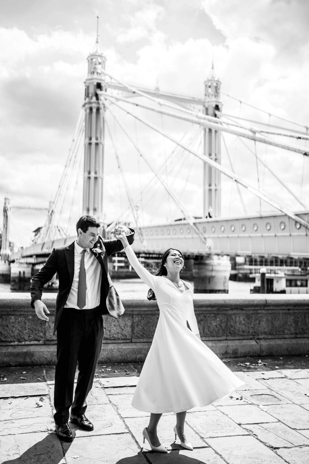 couple doing a twirl on river bank with Albert bridge in background