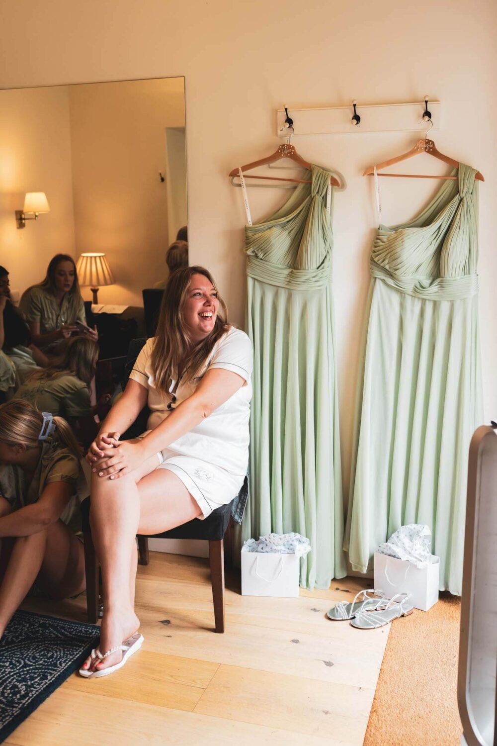 bride smiling looking out of door with bridesmaid dresses hanging up