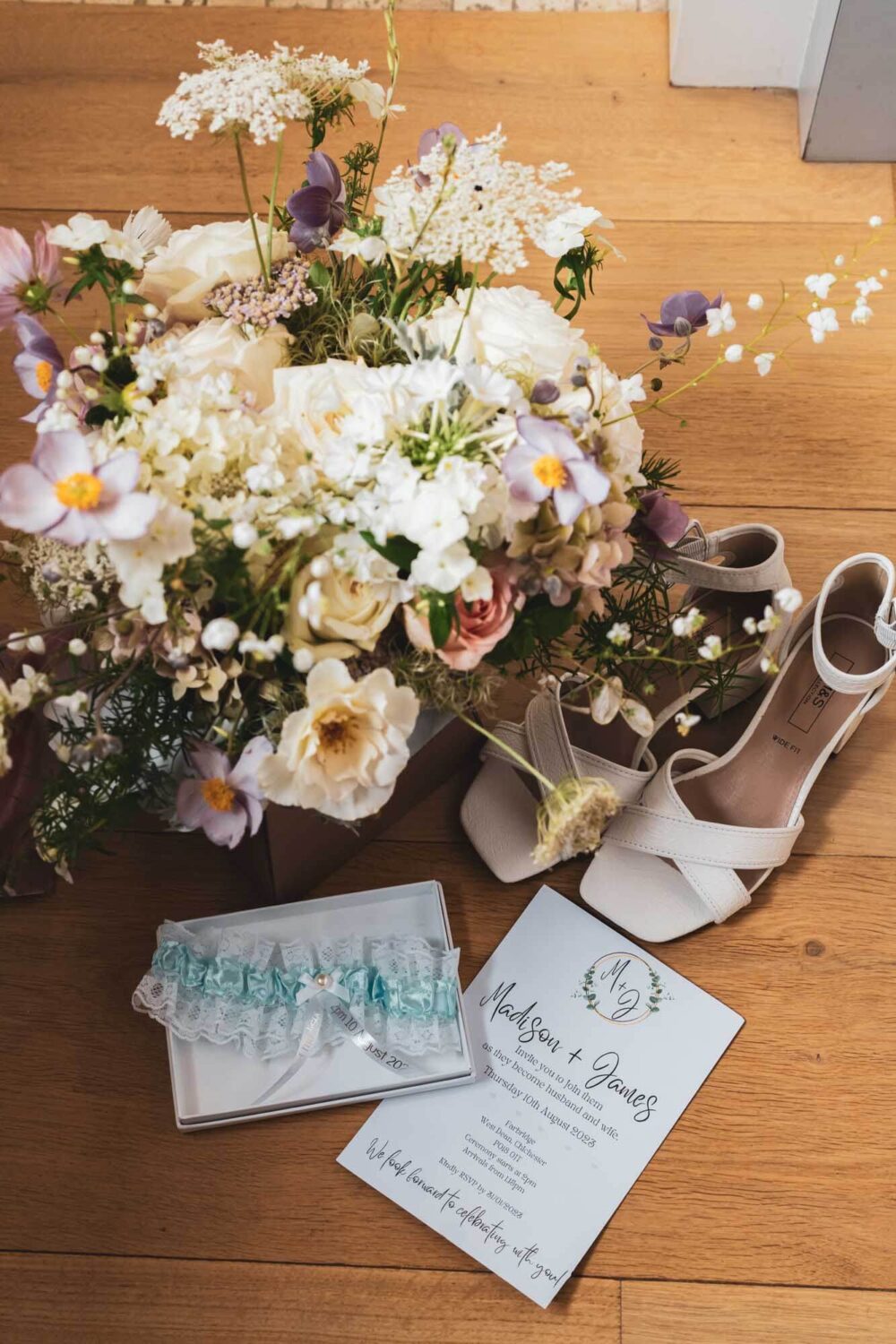 flat lay of flowers, shoes, invitation and garter