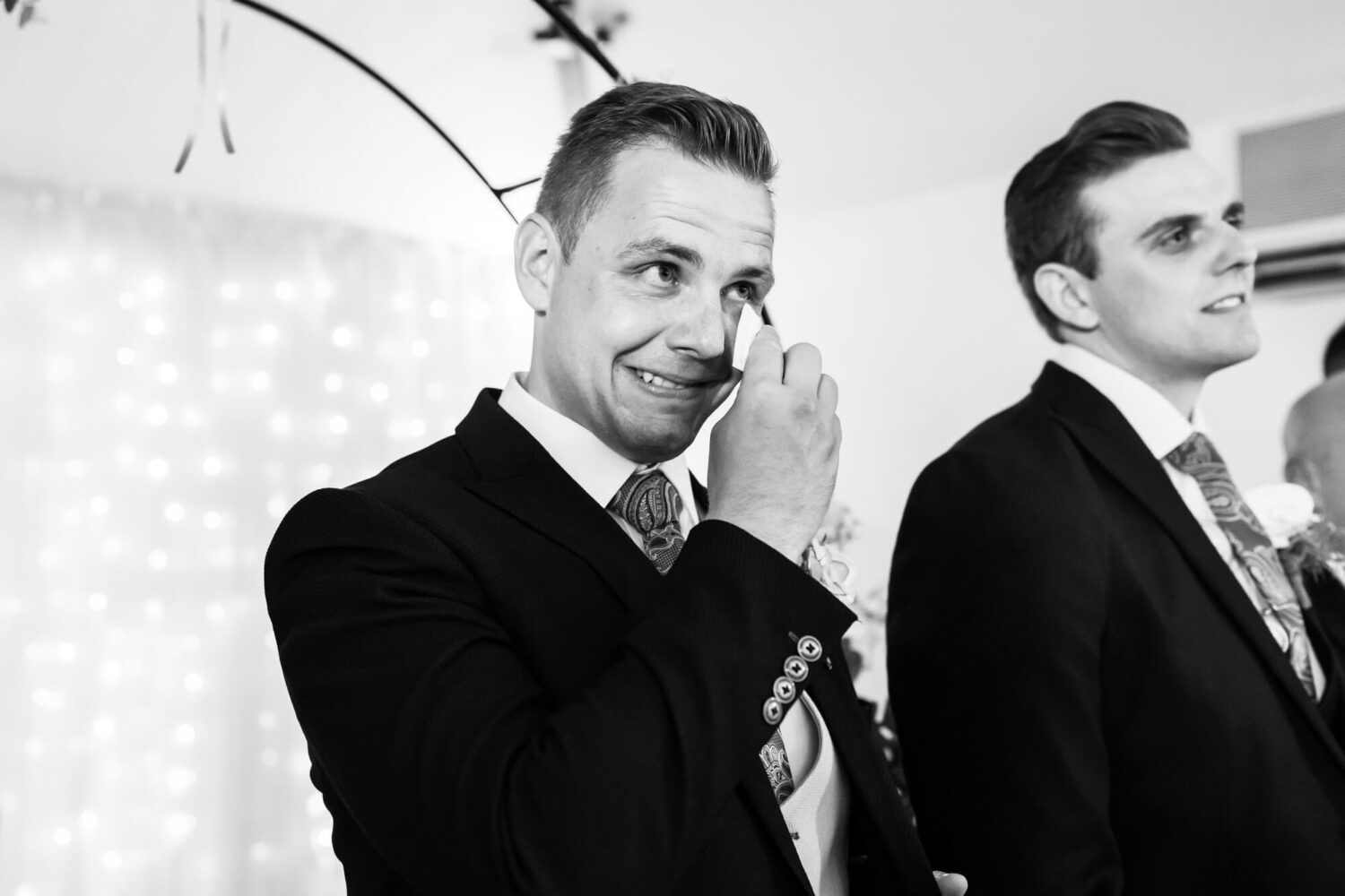 groom wiping away tear with a tissue as his bride walks down the aisle