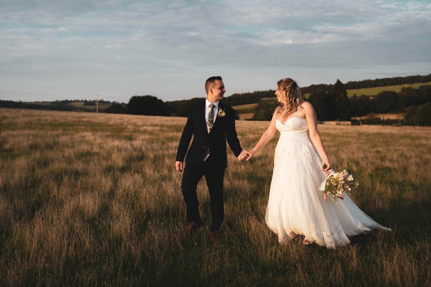 groom leading bride through field at golden hour