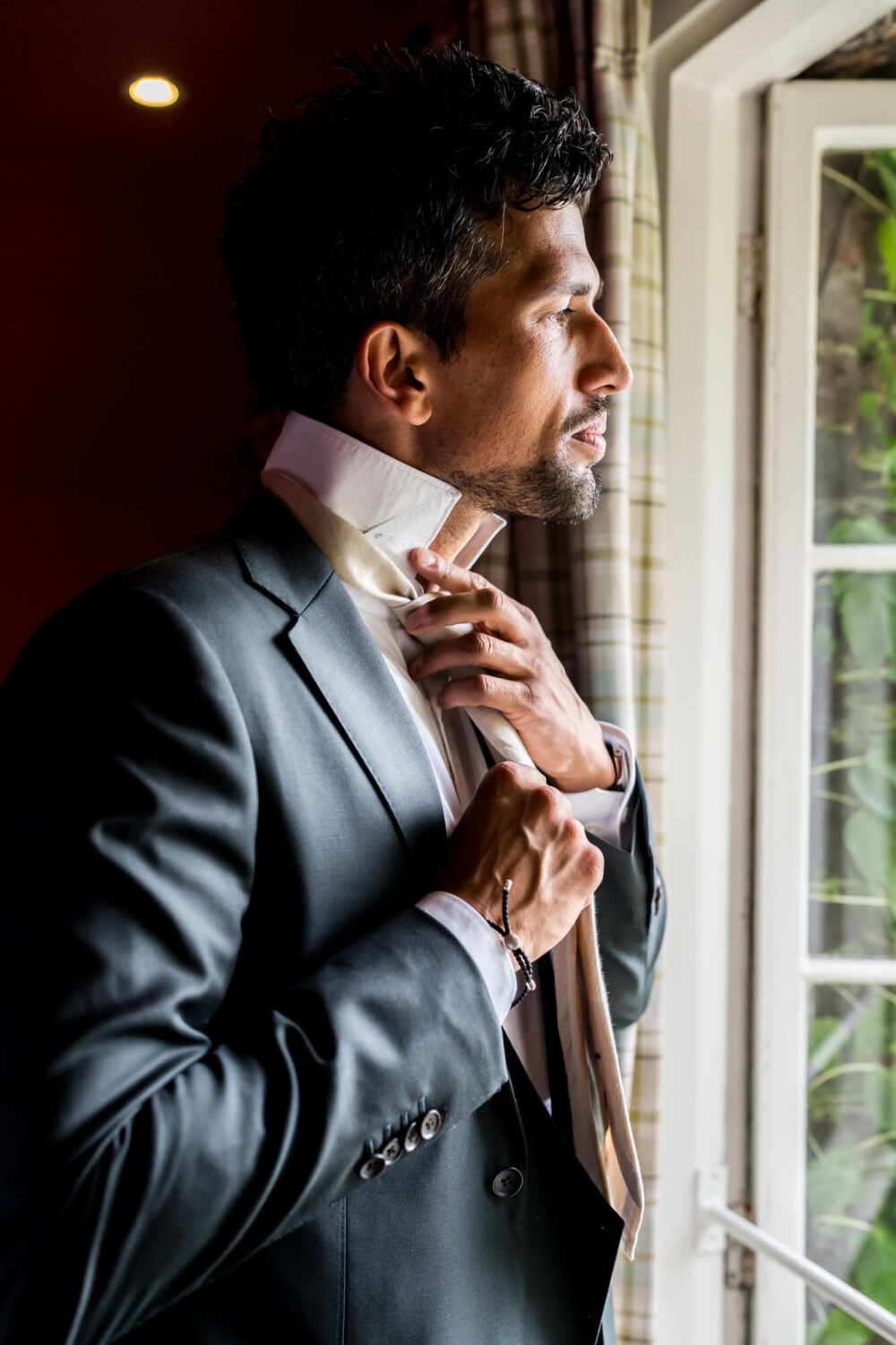 groom doing up his tie looking out of the window