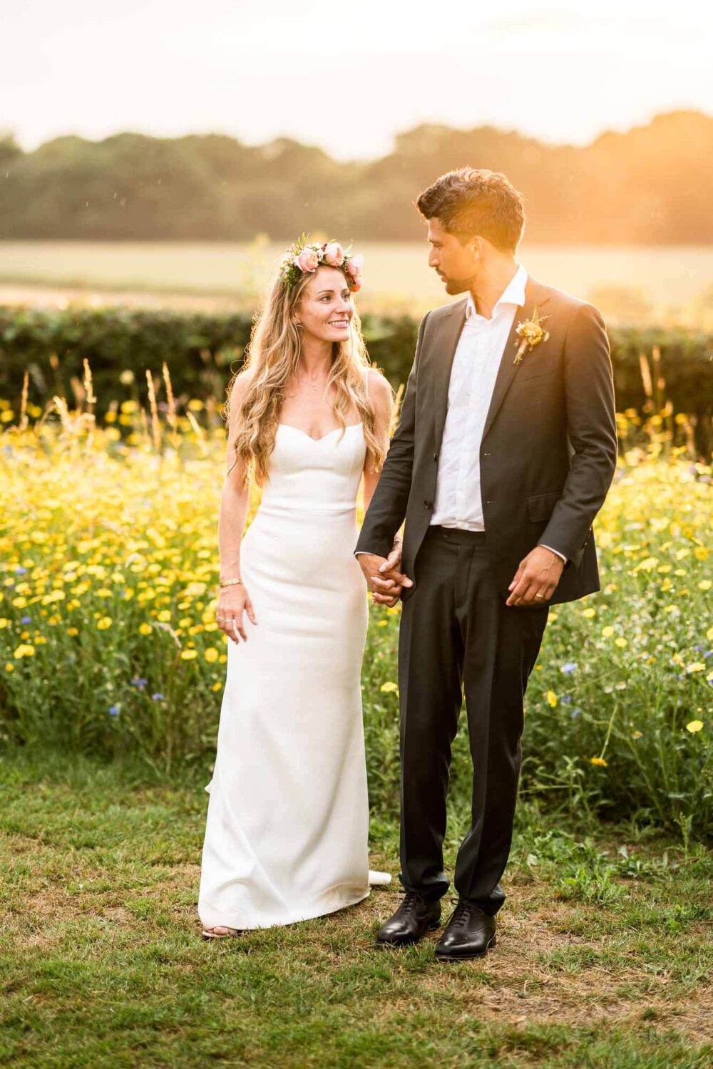 bride and groom walking through field with golden hour