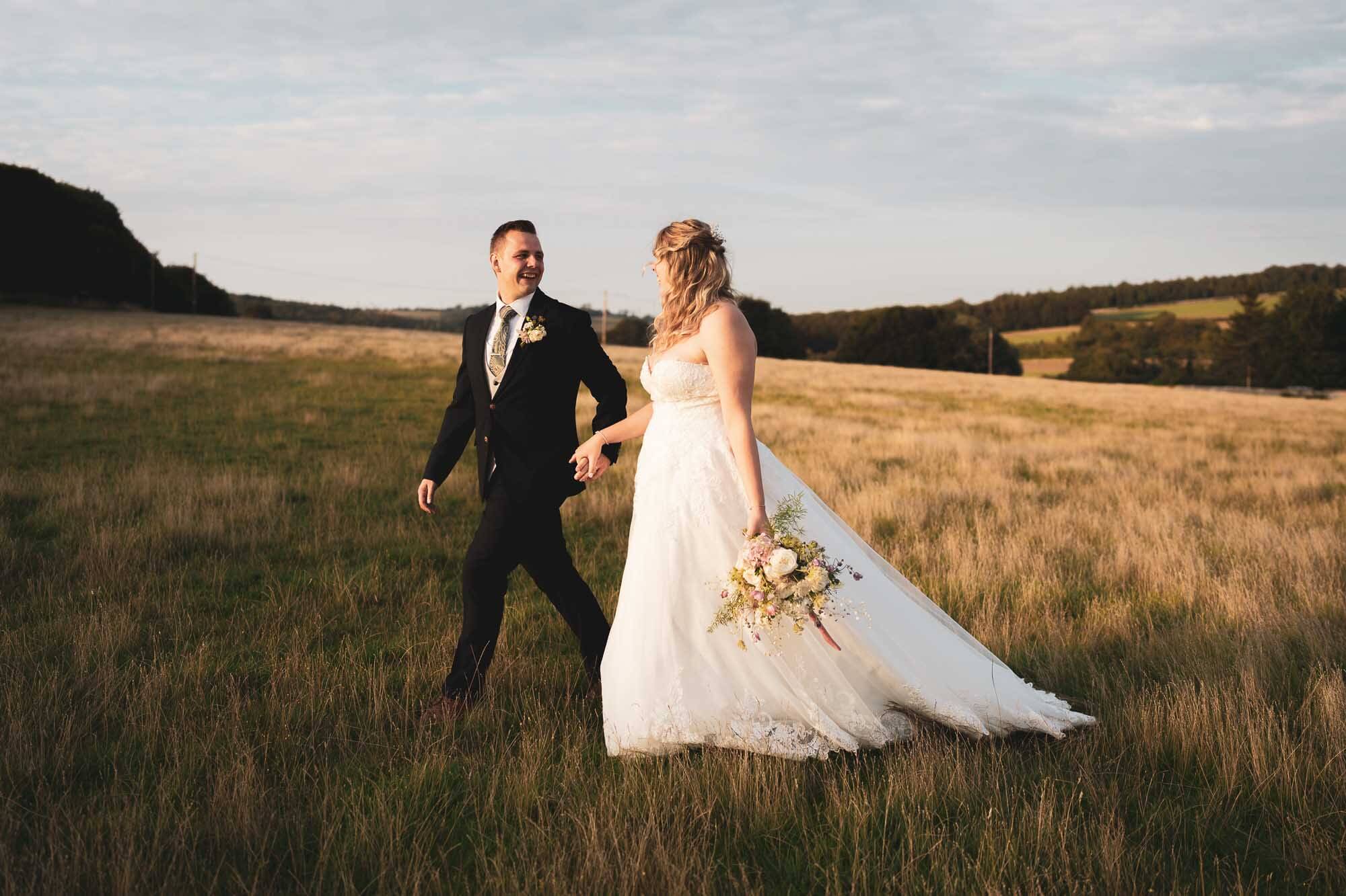 groom leading bride through field during golden hour