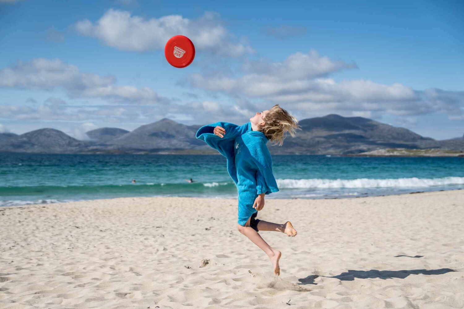 boy throwing read frisbee into the air on luskentyre beach isle of harris