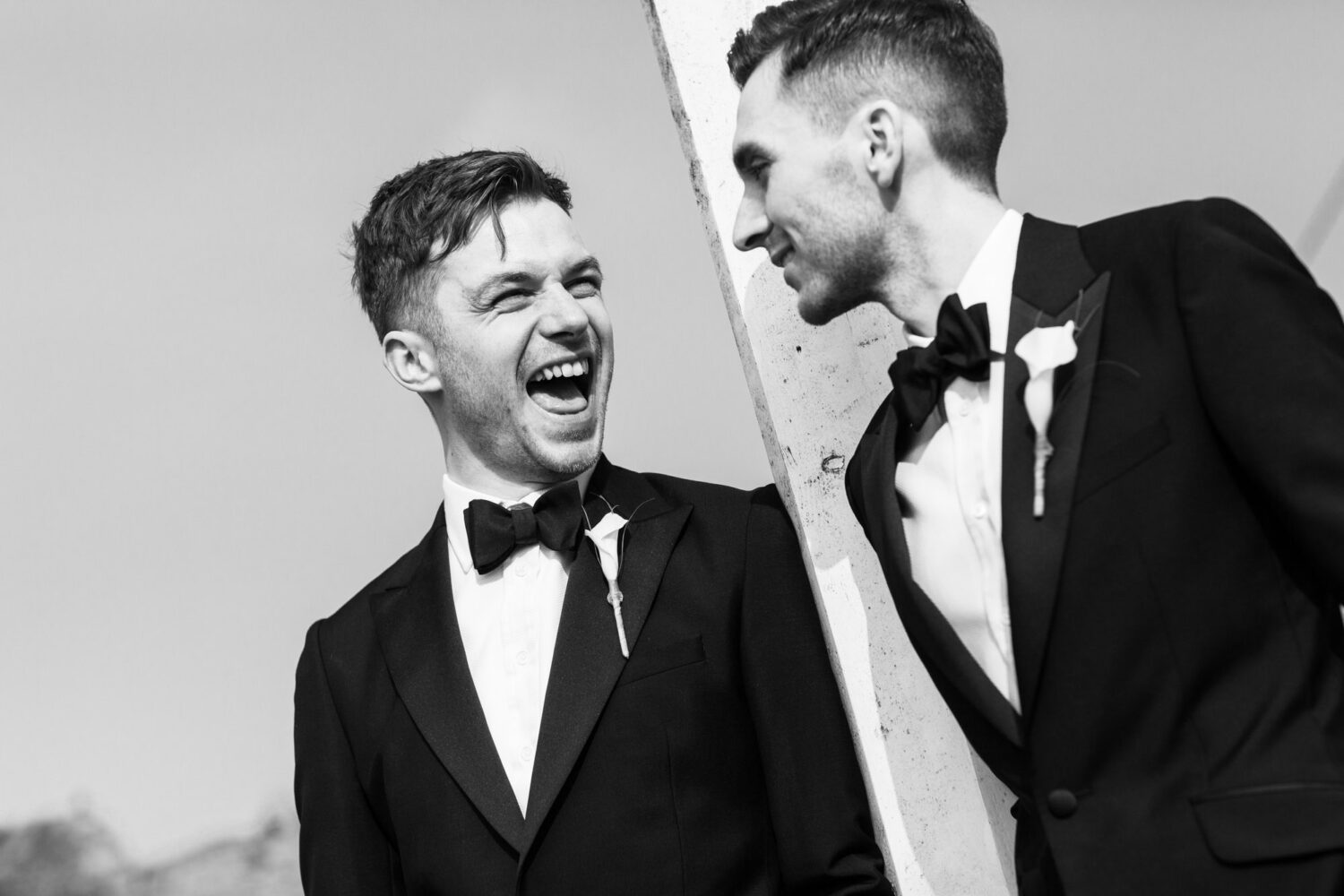 two grooms in tuxedos laughing with each other