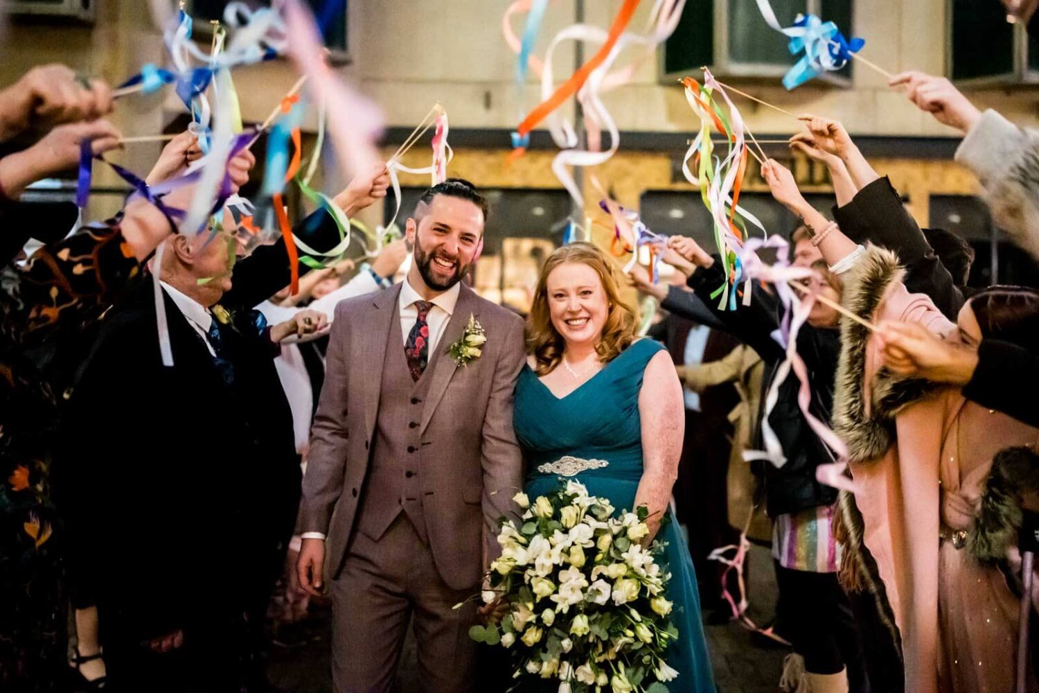 bride and groom walking through line of ribbon waving