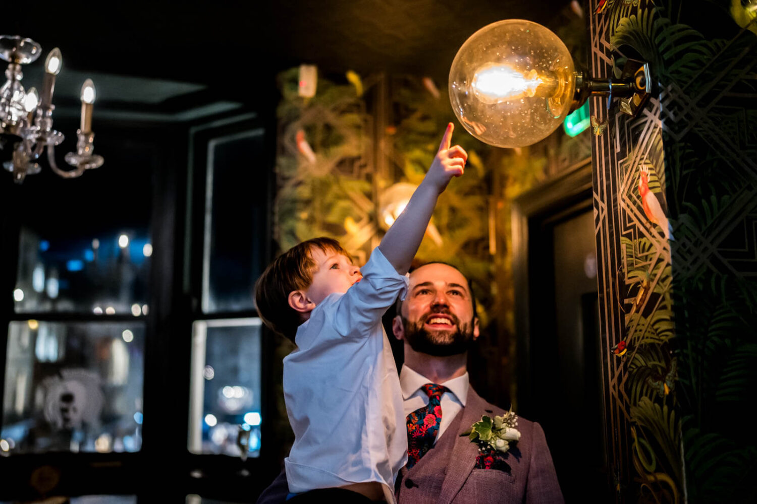 groom holding his kid up to the light to touch it