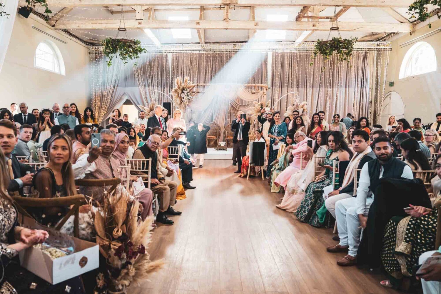 inside of riding school at firle place with boho inspired mandap guests all seated