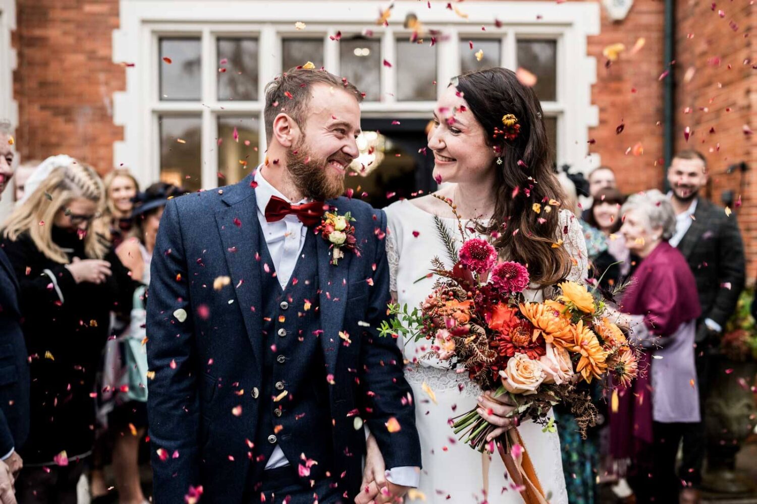groom and bride smiling at each other walking with confetti being thrown at them at highley manor