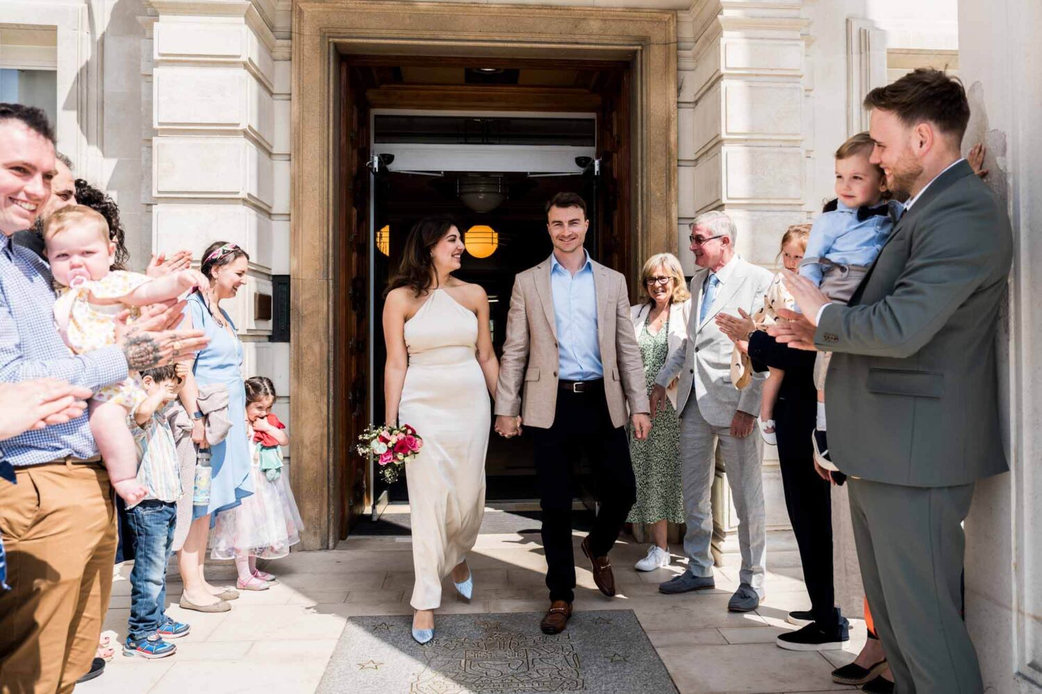 bride and groom walking out of town hall into sunlight london wedding