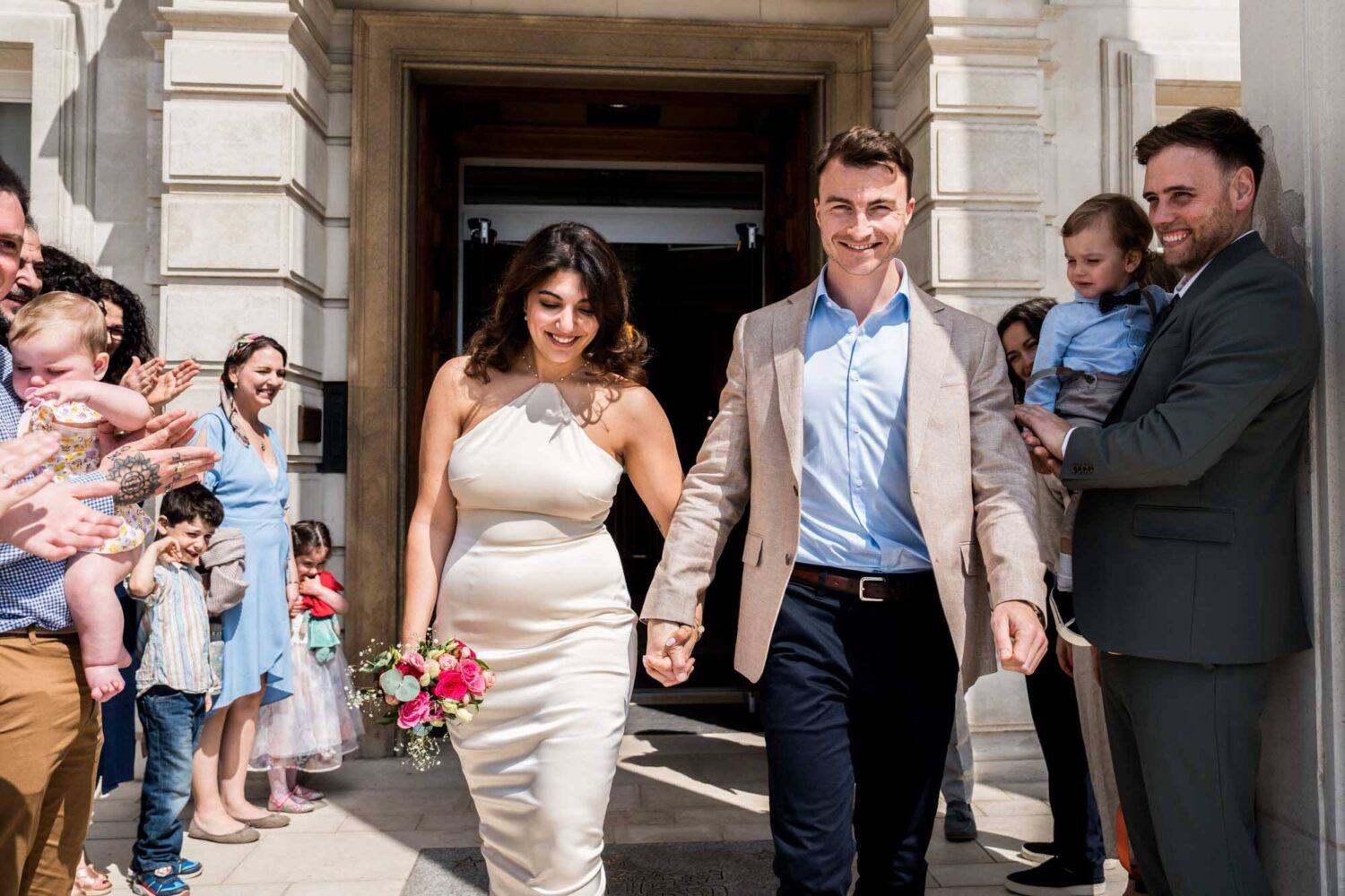 bride and groom walking out of town hall into sunlight london wedding