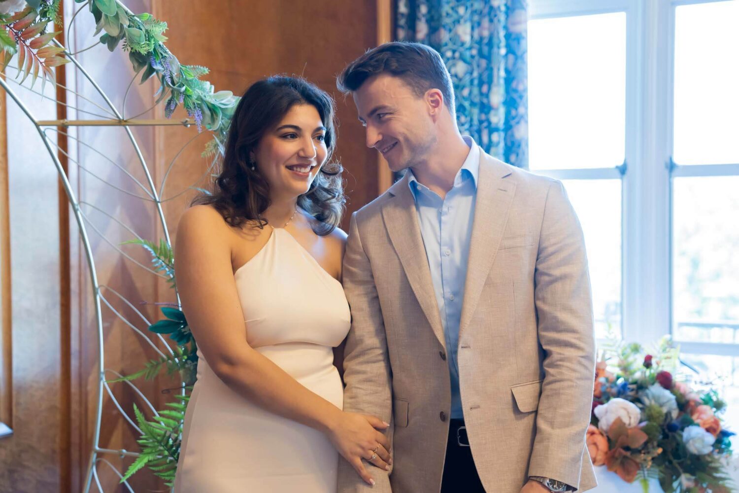 groom smiling at bride looking at her while she holds onto his arms london wedding