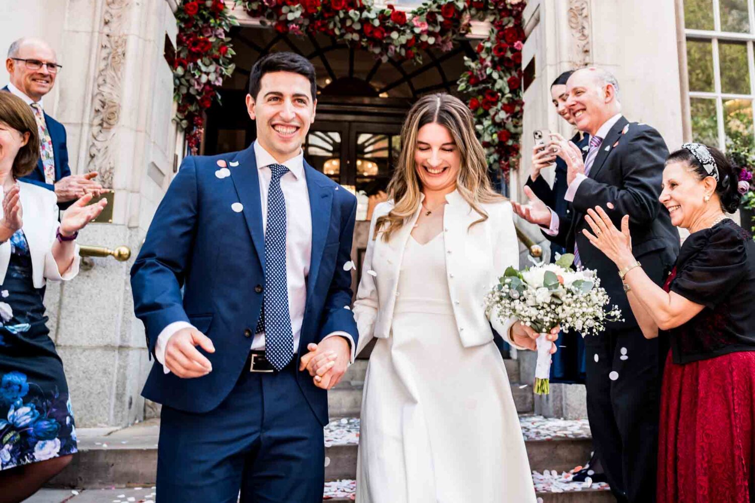 groom smiling looking ahead holding with bride as they walk down steps with confetti being thrown at them