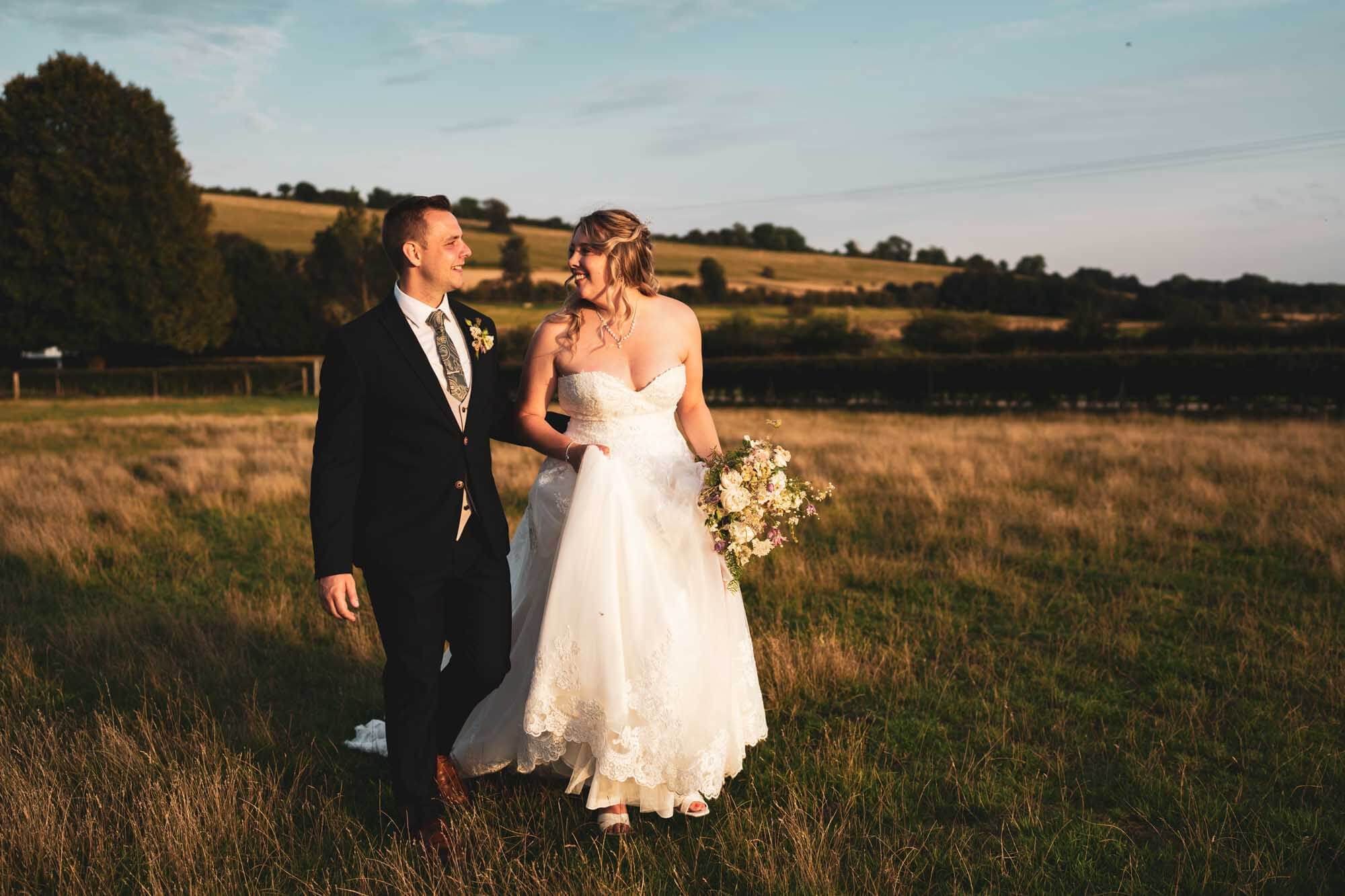 bride and groom walking across field golden hour