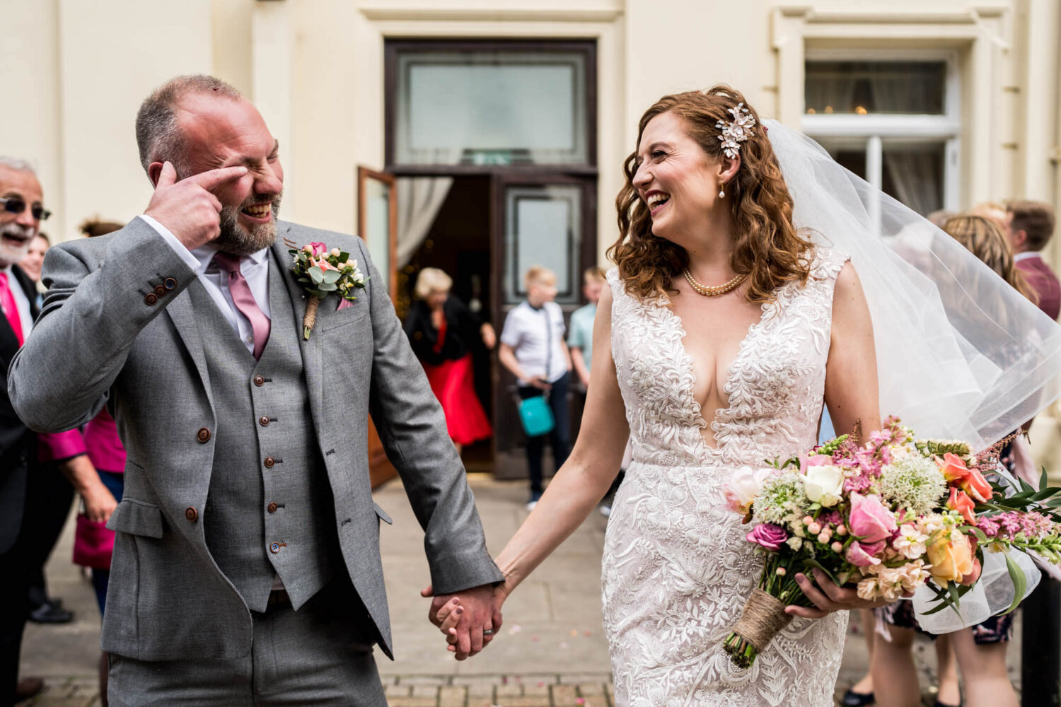 bride laughing as groom wipes confetti from hus eye