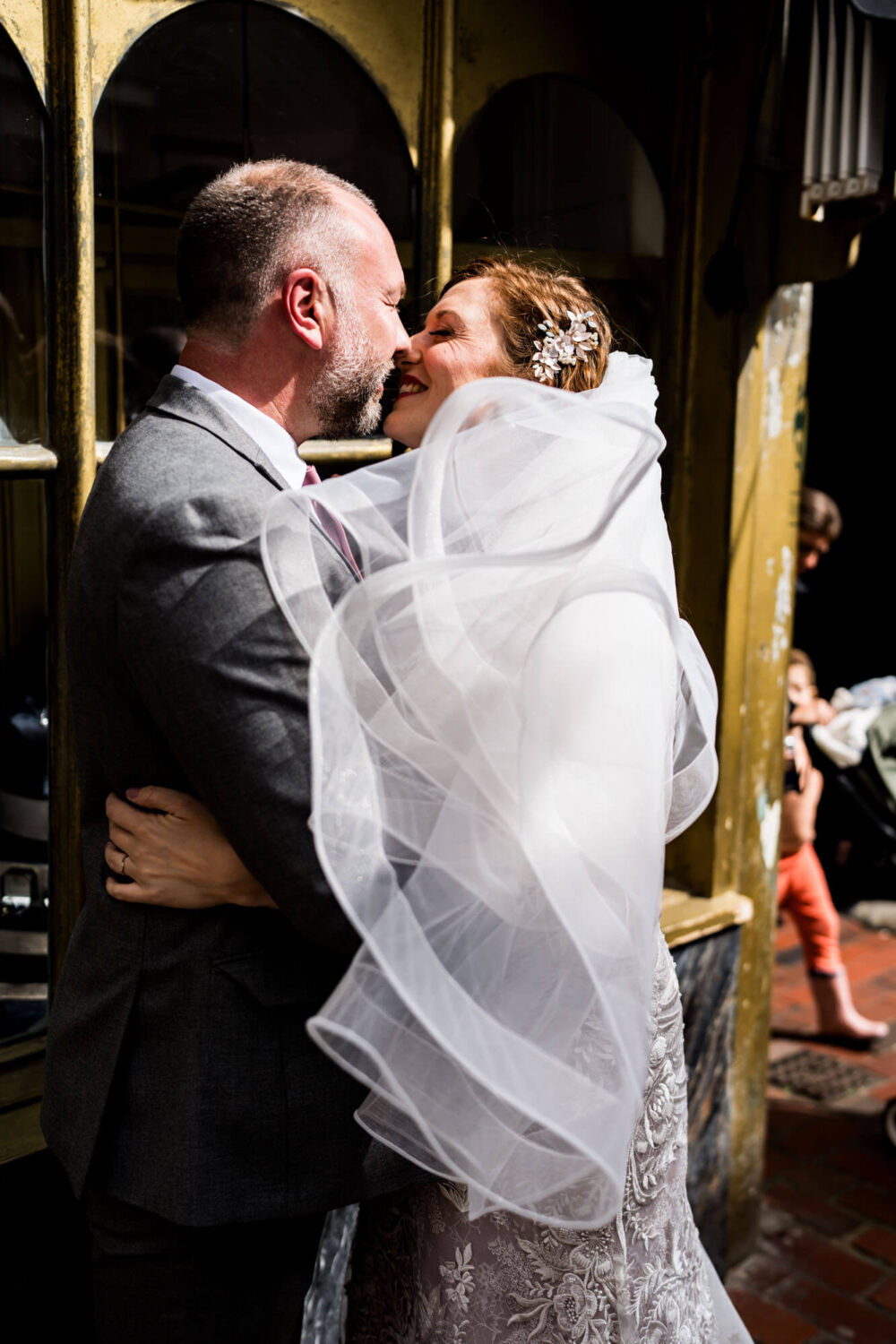 windy veil almost covering bride's face stealing a kiss in the south laines brighton wedding