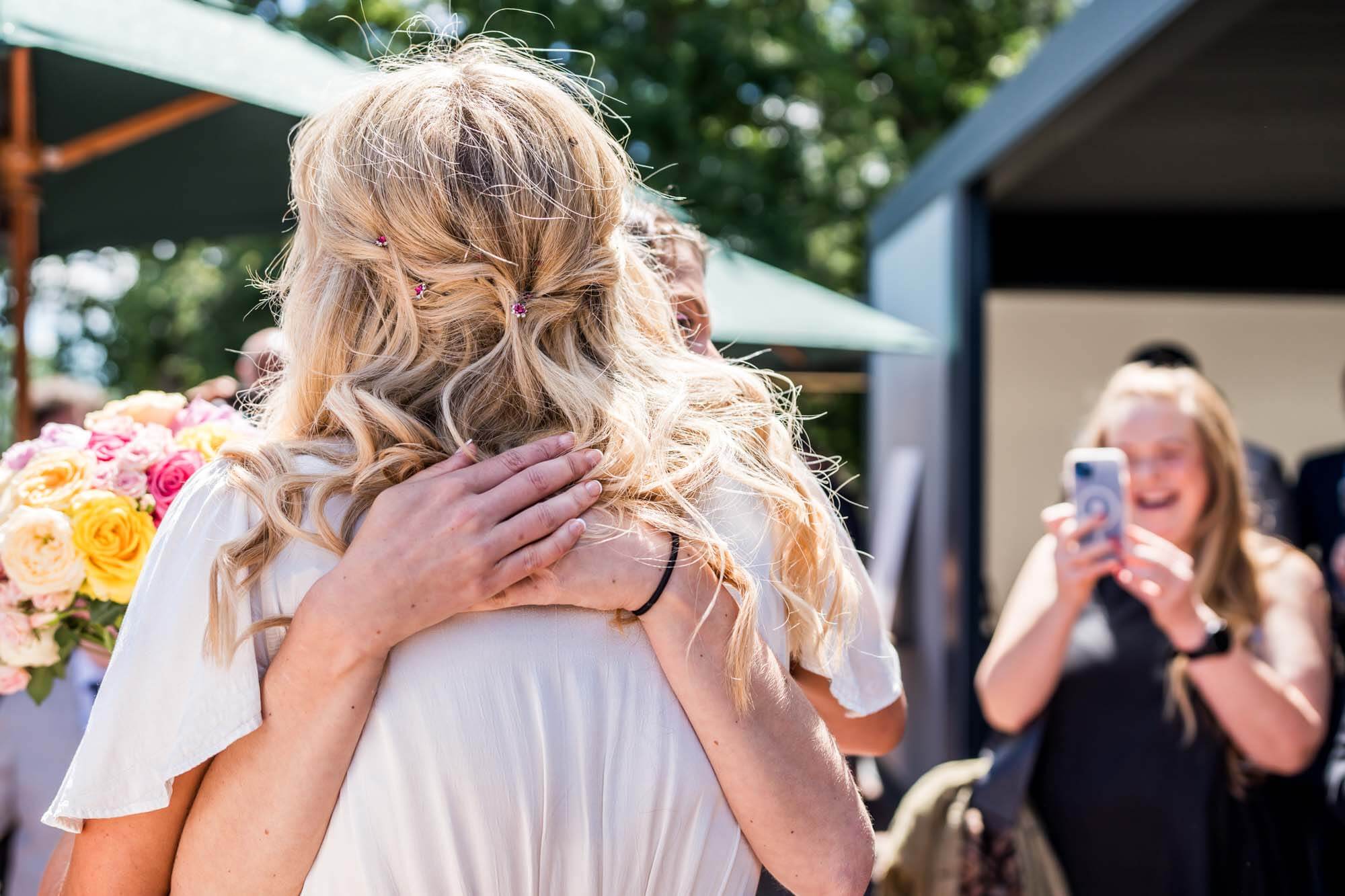 Behind shot of bride and guest hugging.
