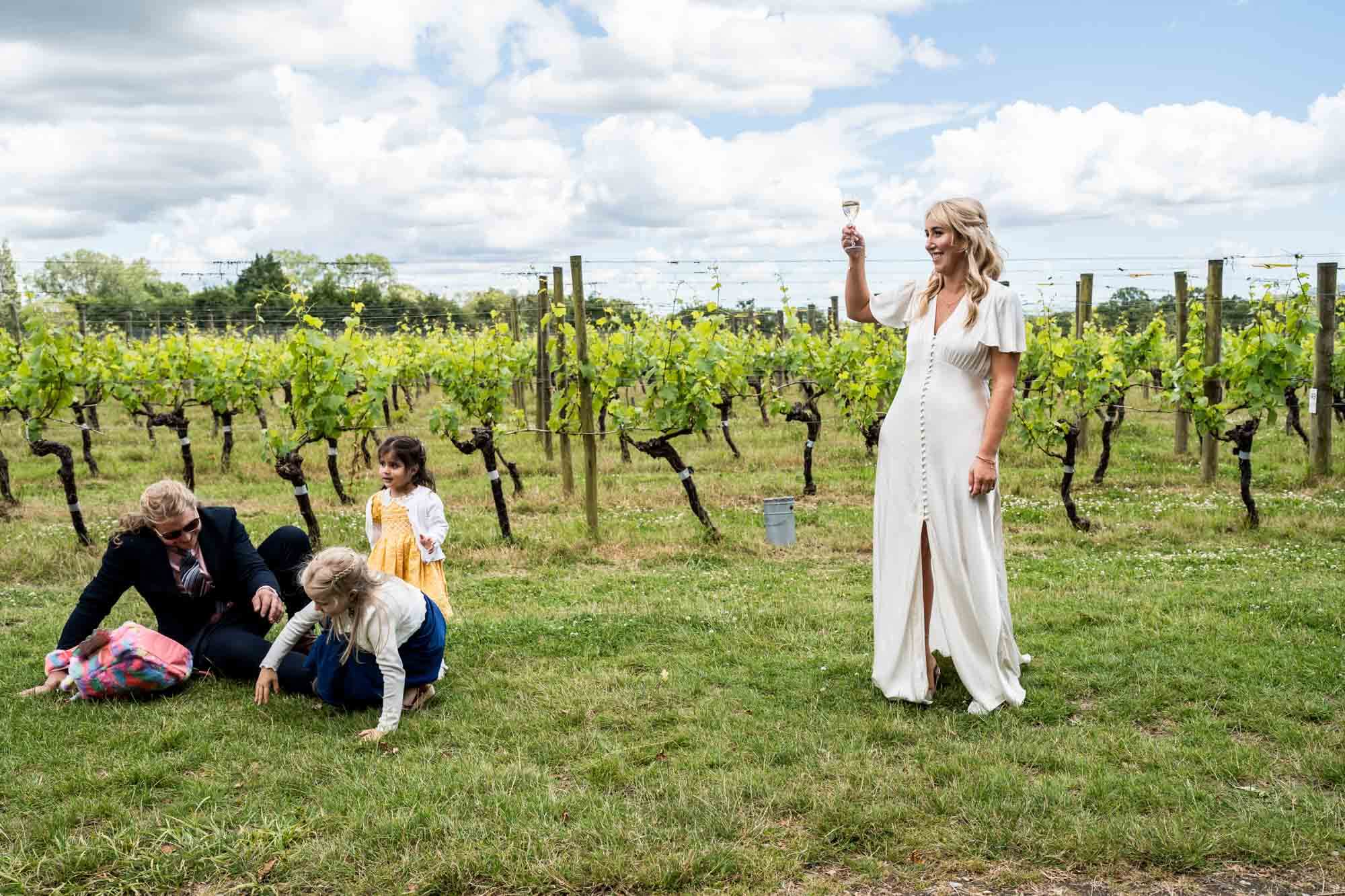 Bride raising champagne and guests on grass.