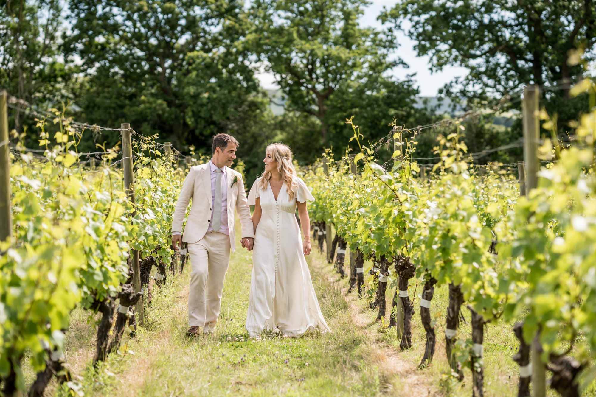 Bride and groom walking down vineyard rows.