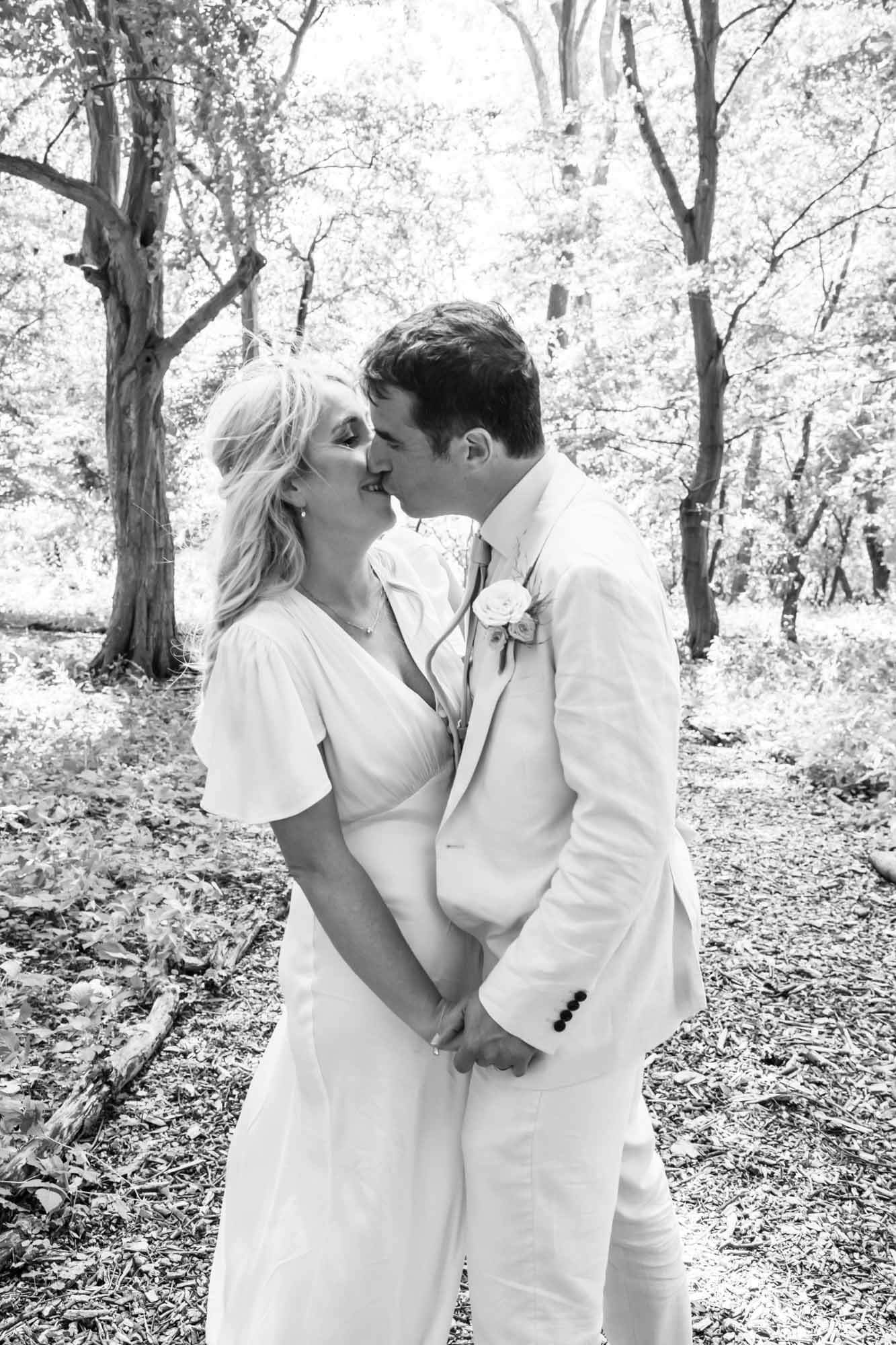 Bride and groom kissing in woods - B&W.