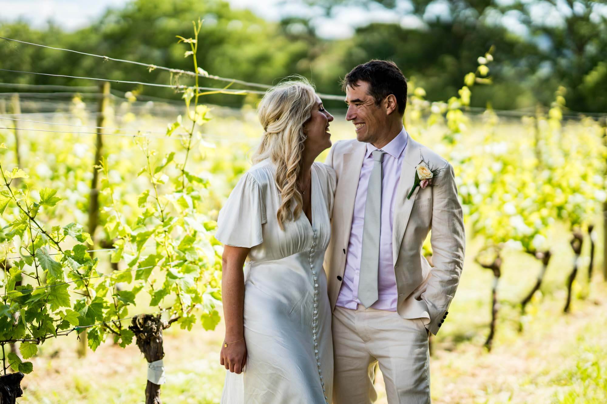 Bride and groom looking at each other in front of vineyard.