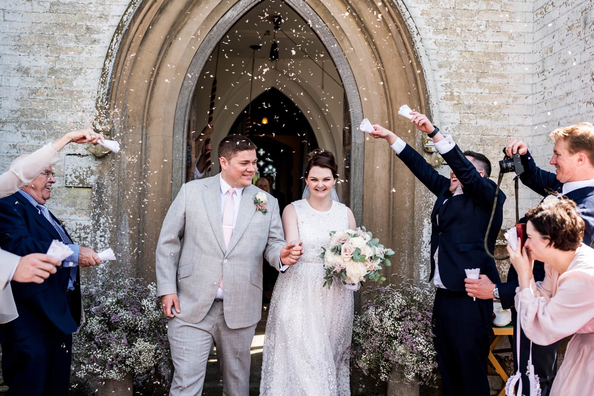 Bride and groom walking out of church into celebratory crowd.
