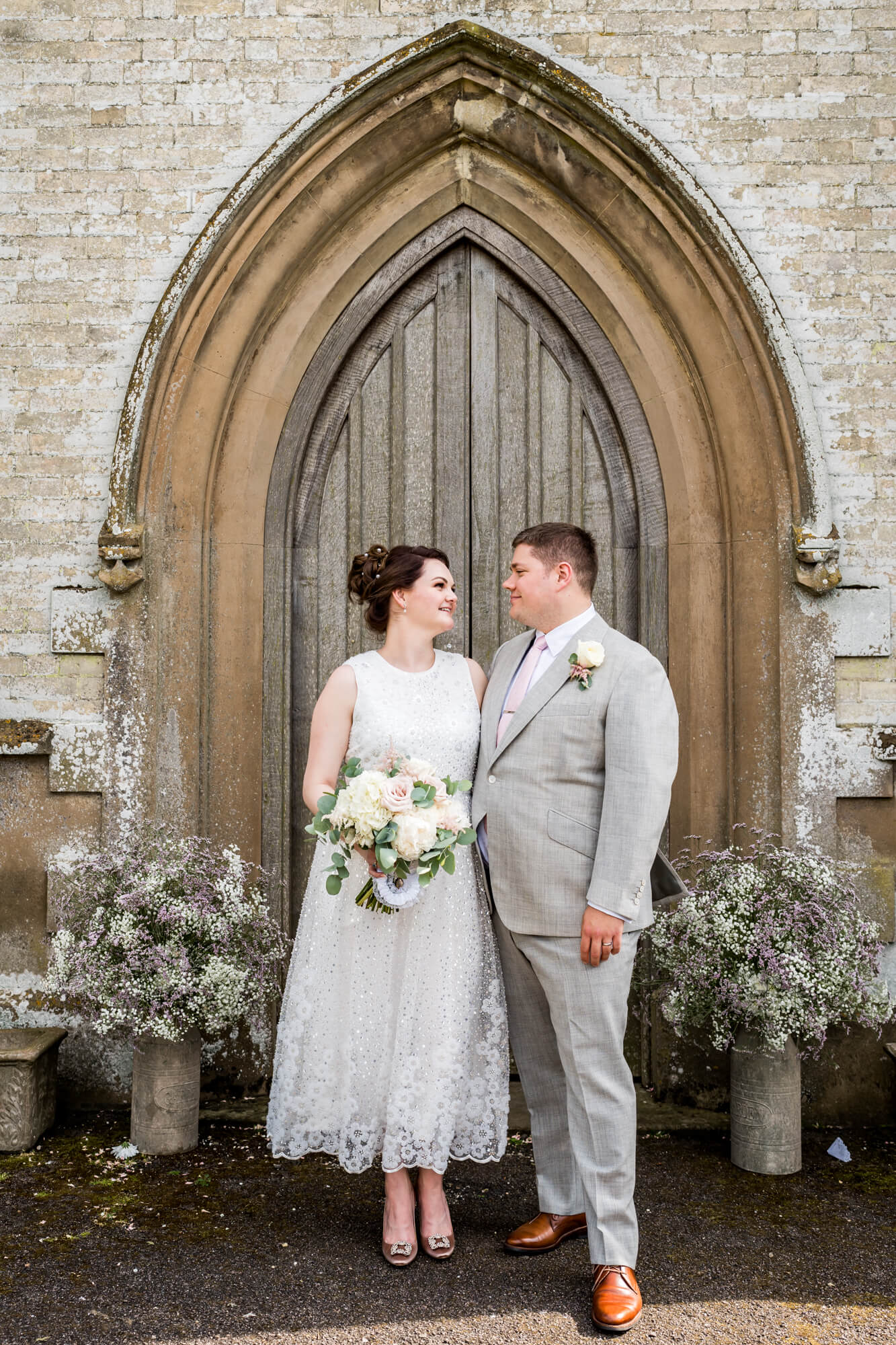 Bride and groom standing in front of church arch with bouquet.