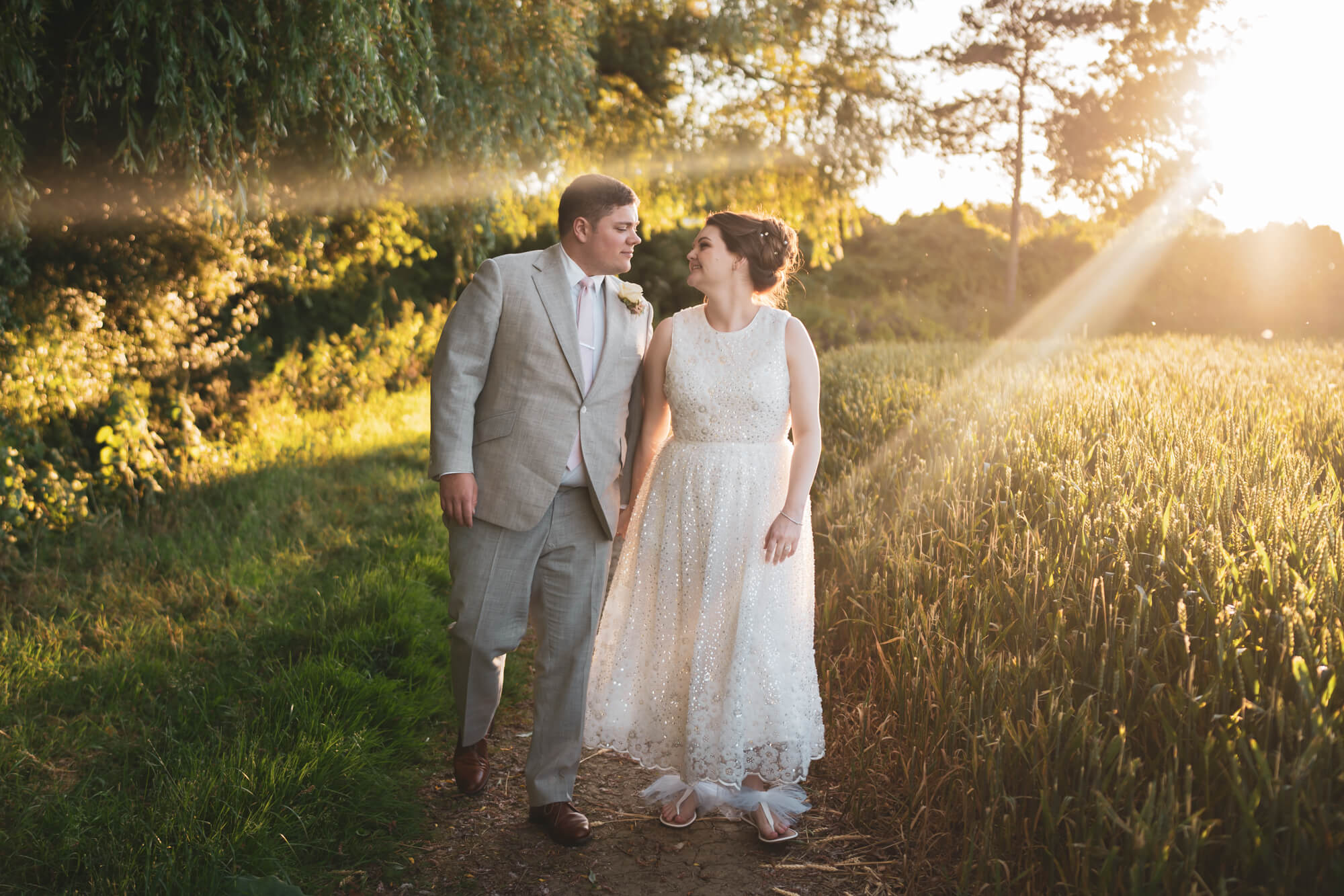 Bride and groom walking alongside field.