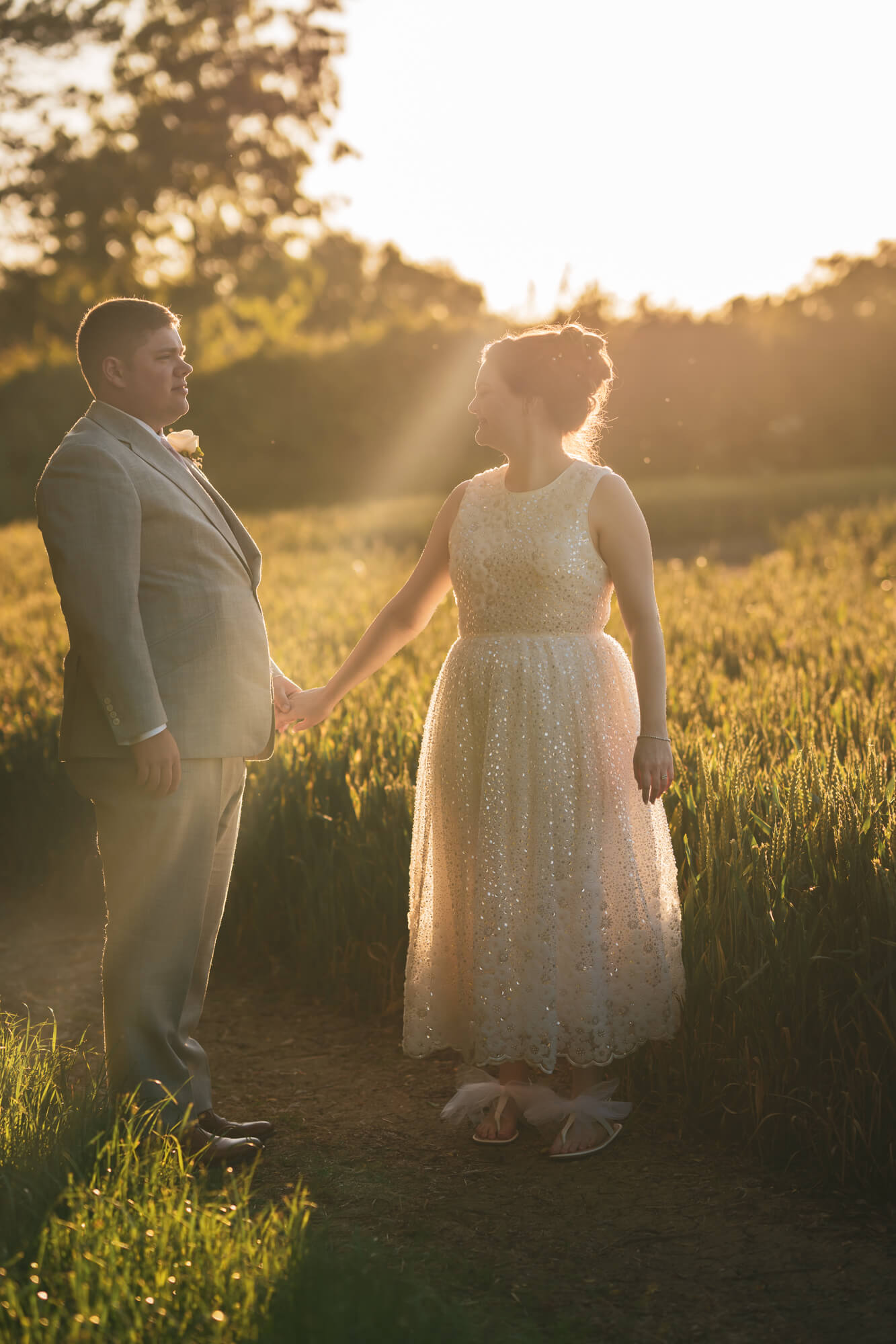 Bride and groom holding hands against sunlight.