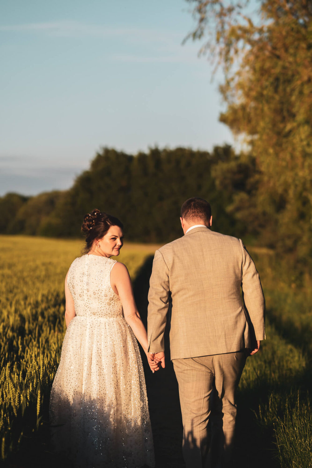 Bride and groom walking away alongside a field.