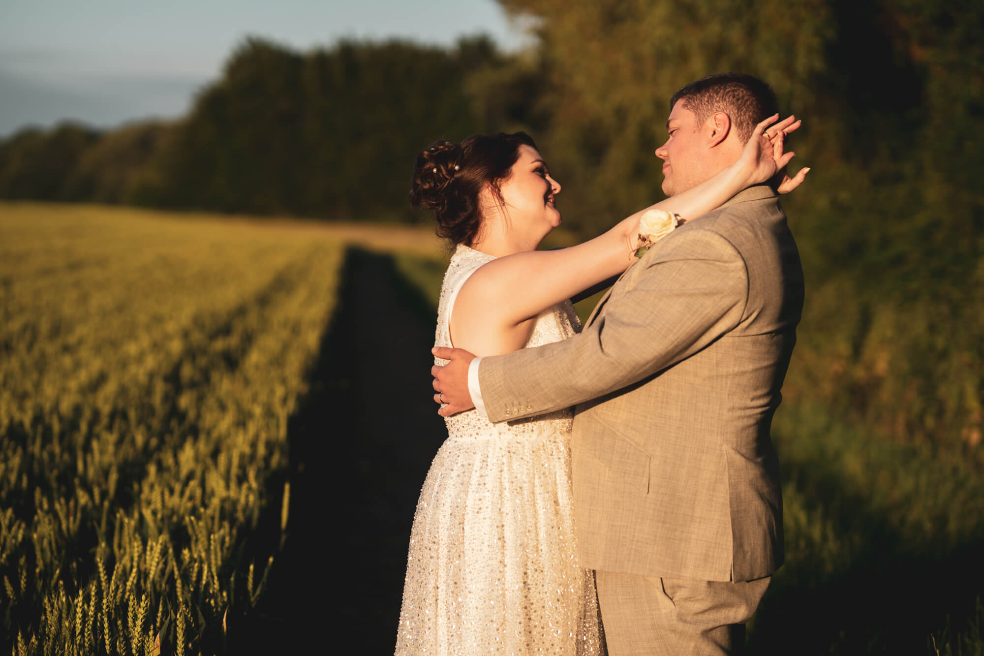 Bride with arms around groom alongside field.