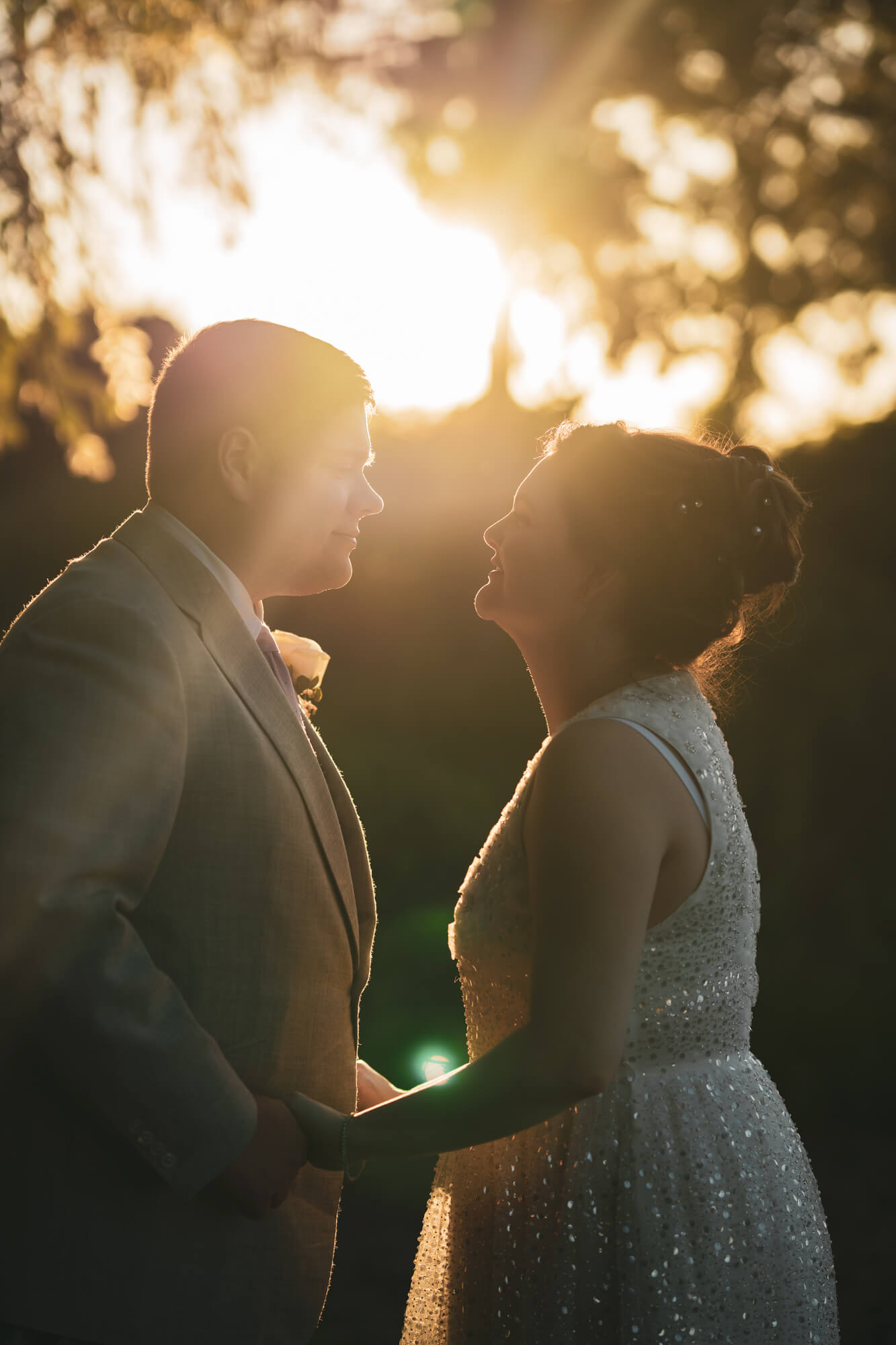 Bride and groom looking at each other against sunlight.