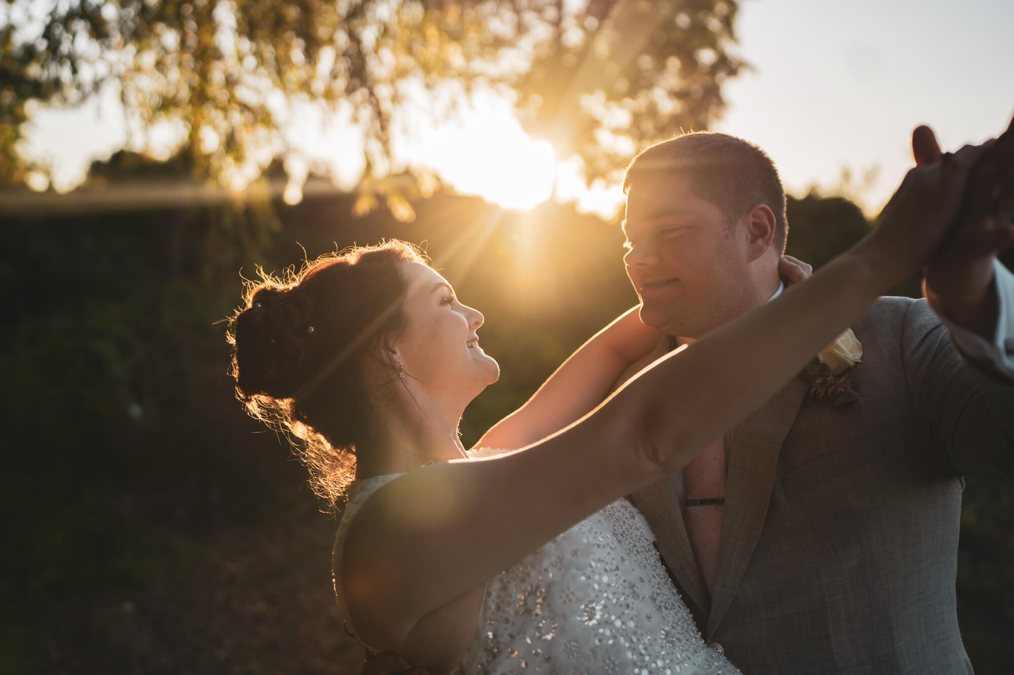Bride and groom dancing against sunlight.