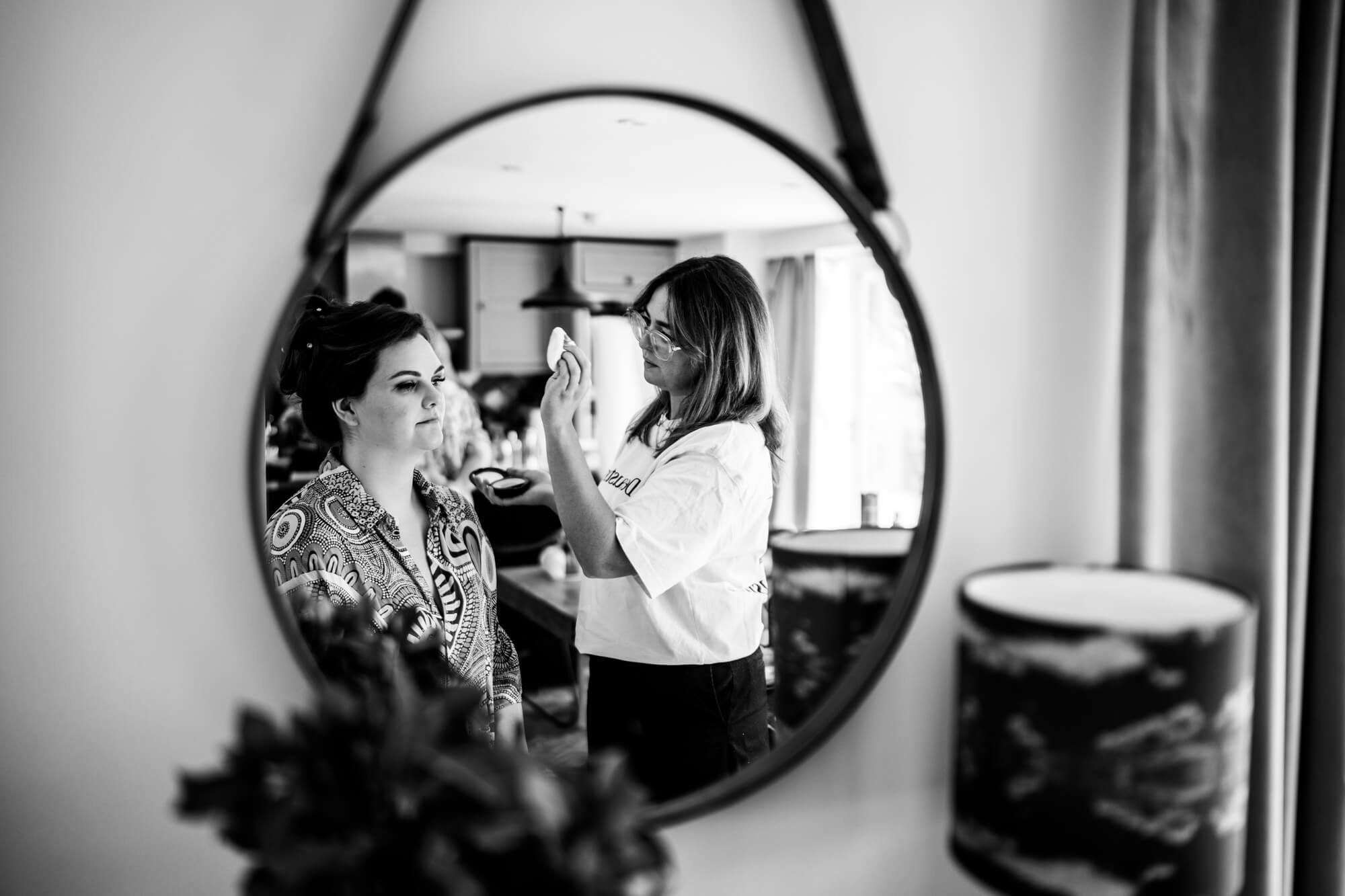 Woman applying makeup to bride in mirror - B&W.
