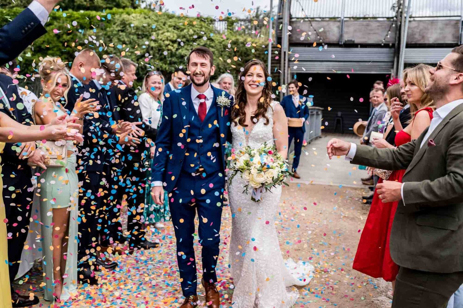 Bride and groom walking through a shower of colourful confetti.