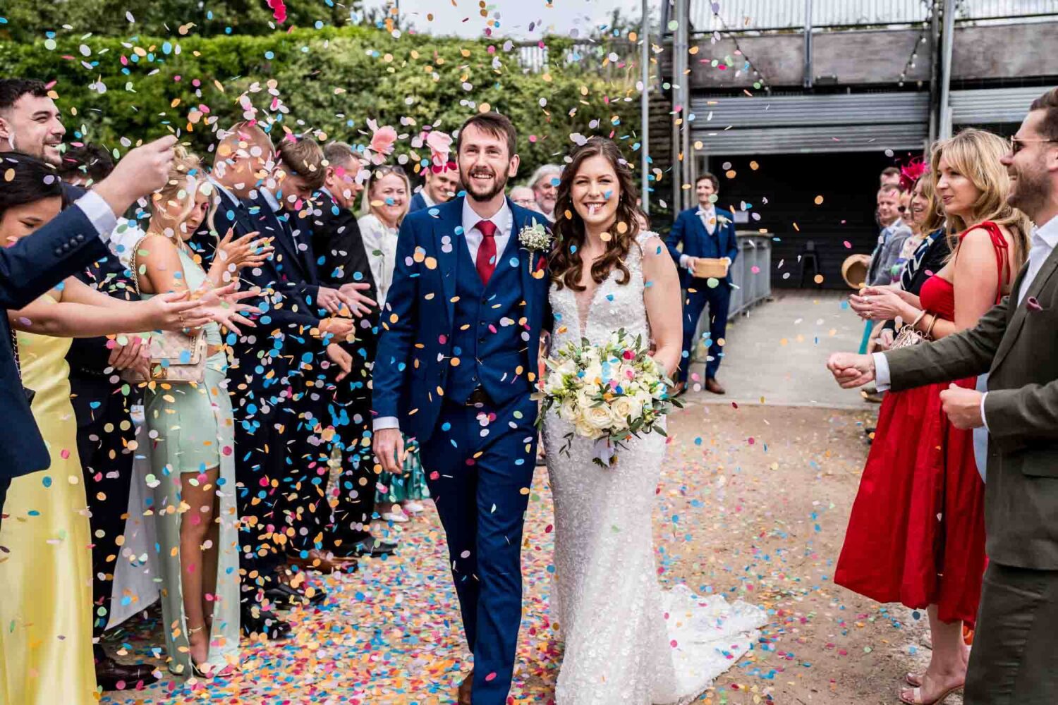 Bride and groom walking through a shower of colourful confetti.