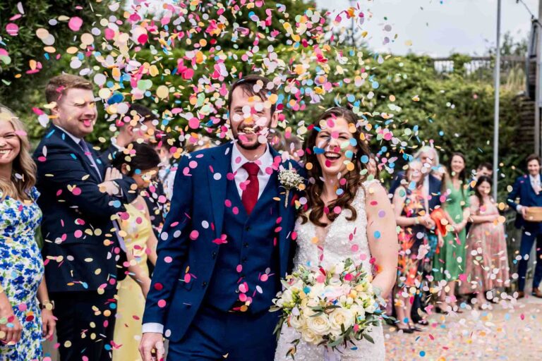 Bride and groom walking through a shower of colourful confetti.