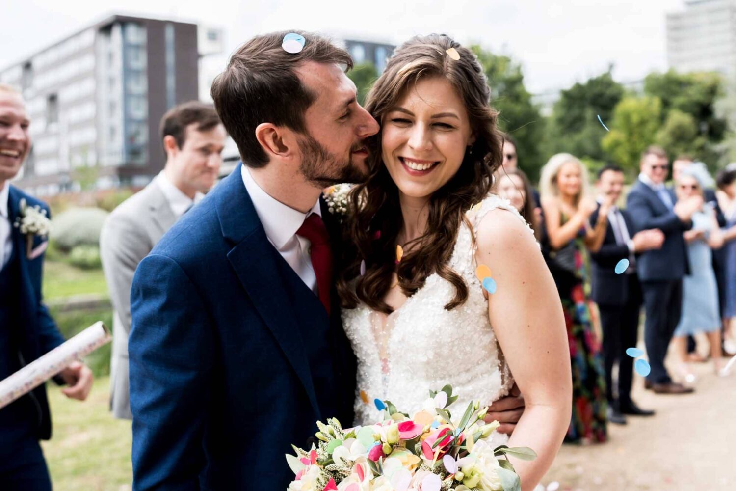 Groom kisses bride with few specs of confetti on their faces.