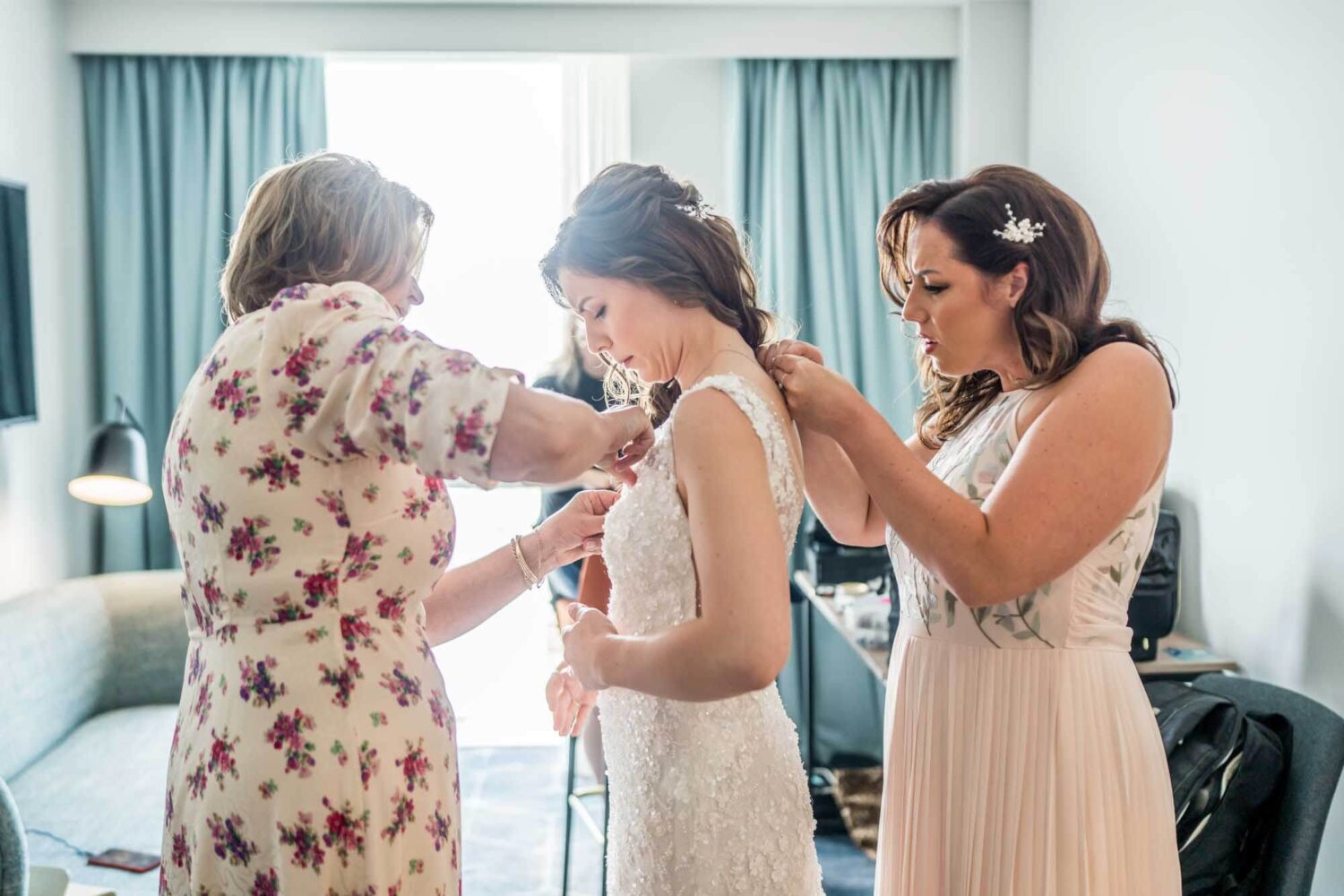 Bride, mother of bride and sister helping bride do up her dress london wedding.
